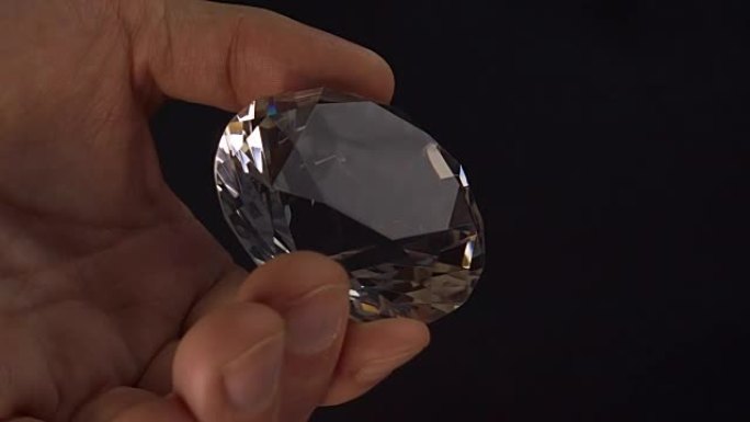 一个人手里拿着一颗巨大的钻石，在光线中看着它