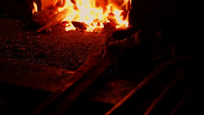 一个铁匠的特写镜头，用这些工具扇动炉子的火焰，防止余烬，火花以慢动作飞向侧面。铁匠手的特写