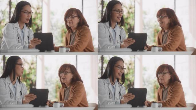 年轻的亚洲医生在健康诊所咨询期间向高级女性患者显示平板电脑上的心脏分析结果。医生坐在医院办公室的桌子