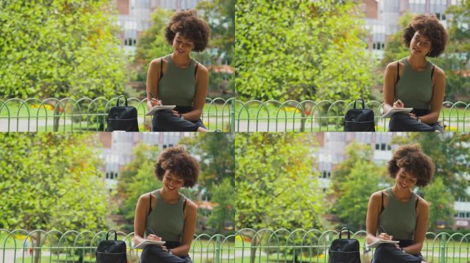 公园里的年轻女子坐在长凳上在笔记本上写字