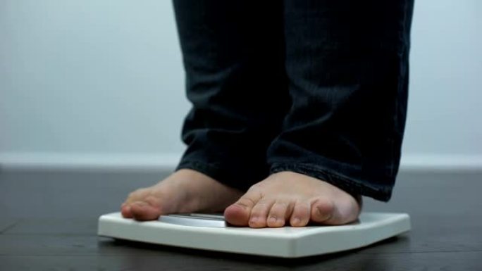 丰满的男性检查体重秤，健康障碍，暴饮暴食的结果