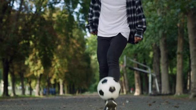 低角度，地面水平射击: 专注于有才华的年轻足球运动员的腿，熟练地玩弄球。时尚的男人在公园里展示他的自