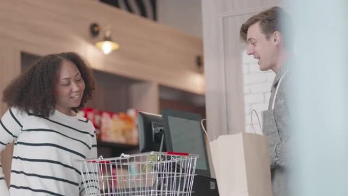 非裔美国年轻女子在购物中心的超市购买消费品，并使用信用卡与收银员进行非接触式付款。享受现代舒适生活的