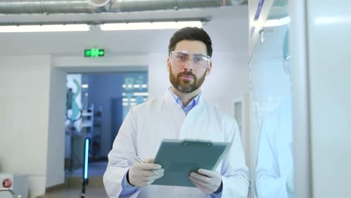 微笑的成熟男人的肖像科学家戴着防护眼镜和手套工作做笔记描述和看着微生物学药物生物化学的相机