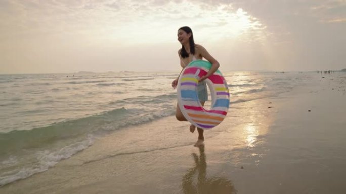 在海滩上跑步的亚洲女孩在白天的晚上使用充气戒指。