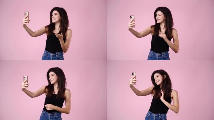 4k视频，可爱的女孩使用手机，在粉色背景上挥手打招呼。