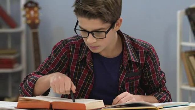 戴眼镜的聪明少年检查书籍中的信息，撰写论文，靛蓝