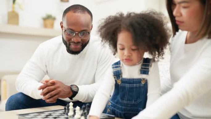 多种族的新手父母正坐在沙发上与女儿下棋。