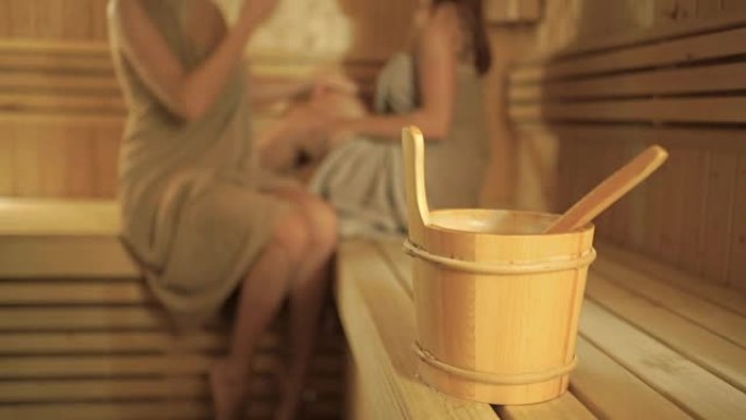 背景模糊的带勺子的木桶，女孩在桑拿浴室放松