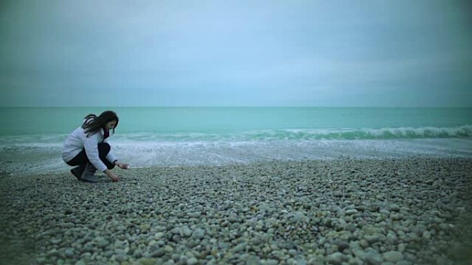 漂亮的女孩把鹅卵石扔进海里，享受美景，泼水