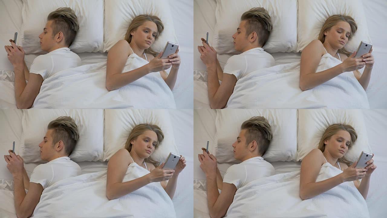 夫妇背靠背躺在床上，用智能手机，社交网络，忽略