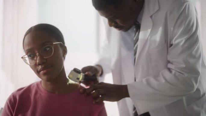 非裔美国皮肤科医生使用皮肤镜在健康检查访问诊所期间，识别出一位美丽的年轻女性皮肤上令人担忧的致癌组织