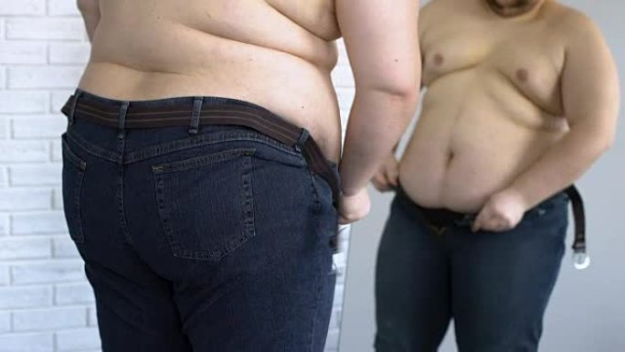 胖男性试图穿上紧身牛仔裤，超重问题，不健康的生活方式