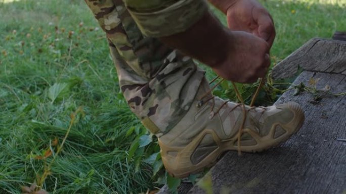 一个穿着迷彩服和战术鞋的无法辨认的男性士兵的脚特写，准备进行军事演习或战斗。男性系鞋带的手