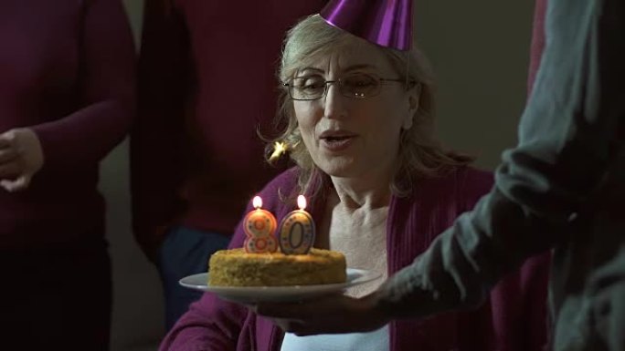 高级妇女在蛋糕上吹蜡烛并微笑，庆祝80岁生日