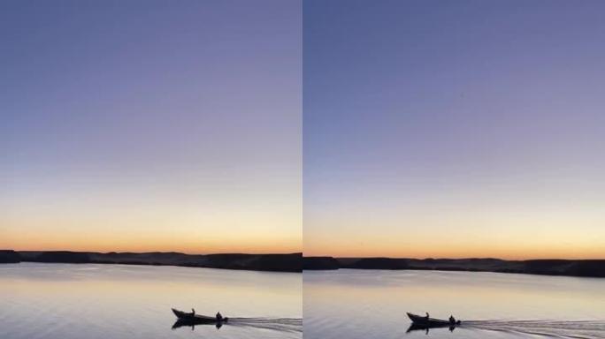 日落时在平坦的湖中独自航行的小船的垂直视图。黄金时刻