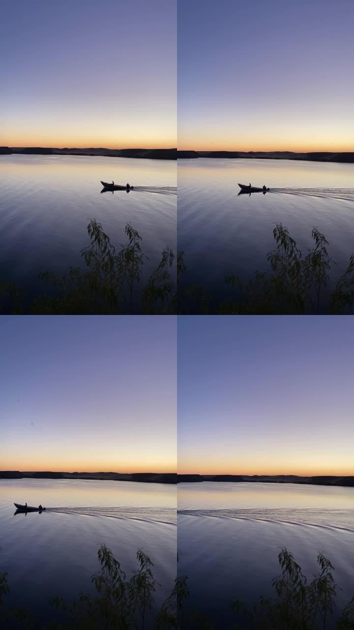 日落时在平坦的湖中独自航行的小船的垂直视图。黄金时刻