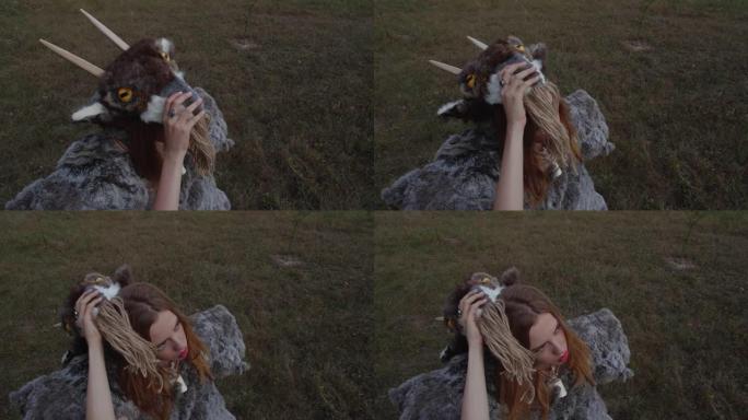 近距离拍摄金发女孩的肖像，她穿着一种异教动物般的皮毛，由皮肤制成，站在草地的背景下，戴着带角的山羊面