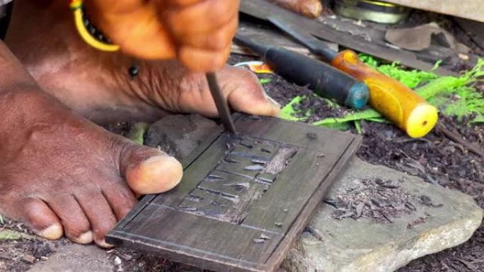 坦桑尼亚当地男子用脚趾手指拿着一块石板，用金属凿子和锤子雕刻安娜字。旅行和工匠的日常工作4k概念镜头