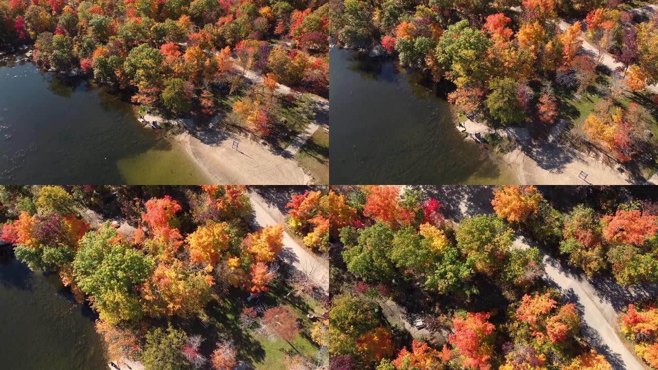 空中无人驾驶飞机在露营地上空飞行，周围环绕着五颜六色的秋天树木，旁边是镜面湖，人们站着观察美丽，加拿