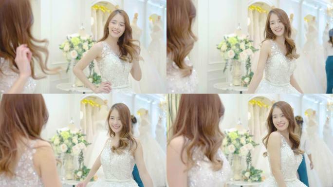 年轻的亚洲女子微笑着在商店试穿婚纱，亚洲新娘照镜子看美丽，年轻的女性检查美丽的倒影，幸福的微笑结婚，