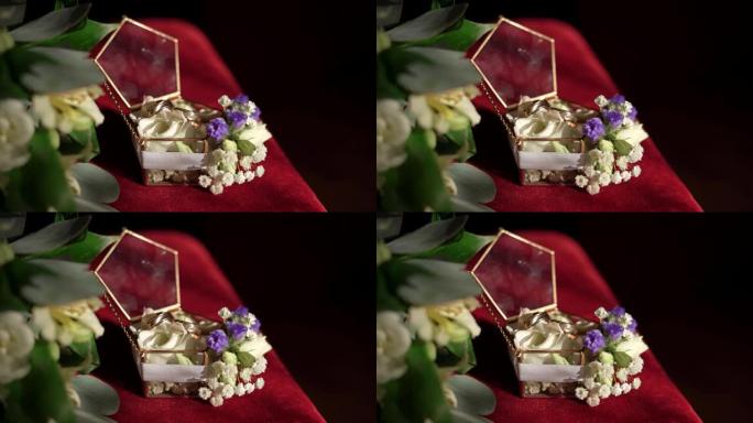 玻璃盒子里有两个金色订婚戒指，红色表面有一个白色和蓝色花朵和叶子的树枝。订婚戒指，复制空间