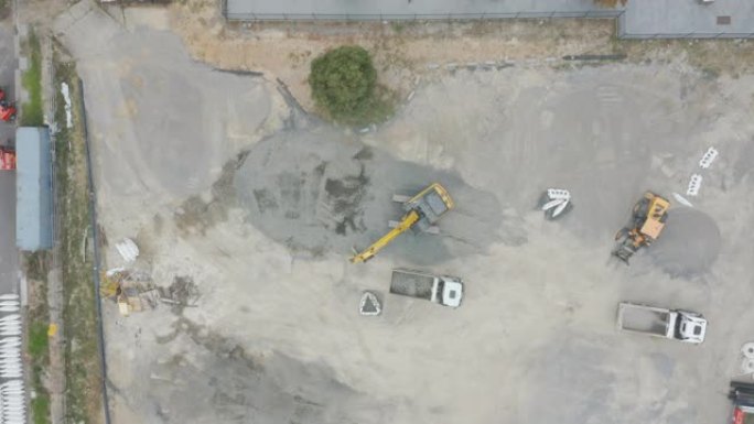 挖掘机在裸露的建筑工地上缓慢地将土壤移动到卡车装载托盘上。