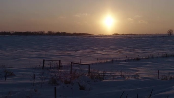 在冰冻的积雪覆盖的田野上拍摄朦胧的日落