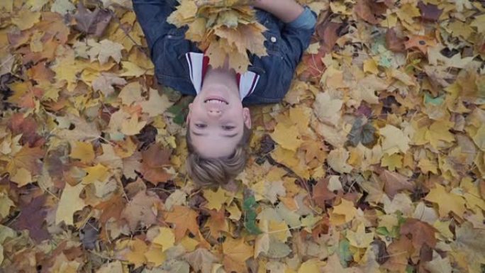 微笑的男孩躺在秋天森林的黄叶上