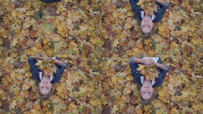 微笑的男孩躺在秋天森林的黄叶上
