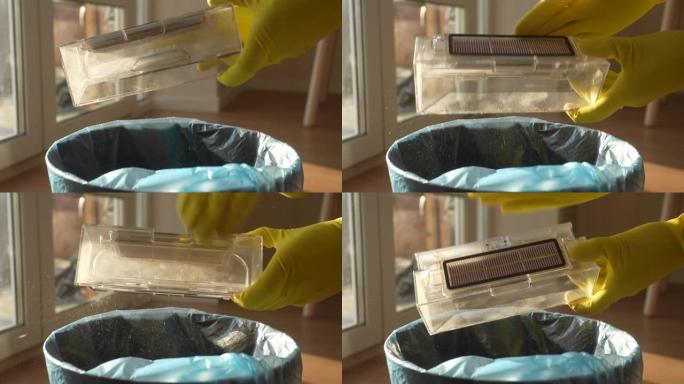 戴着橡胶手套的无法辨认的管家男子的特写侧视图，在垃圾桶上摇晃机器人真空吸尘器的垃圾箱，慢动作。