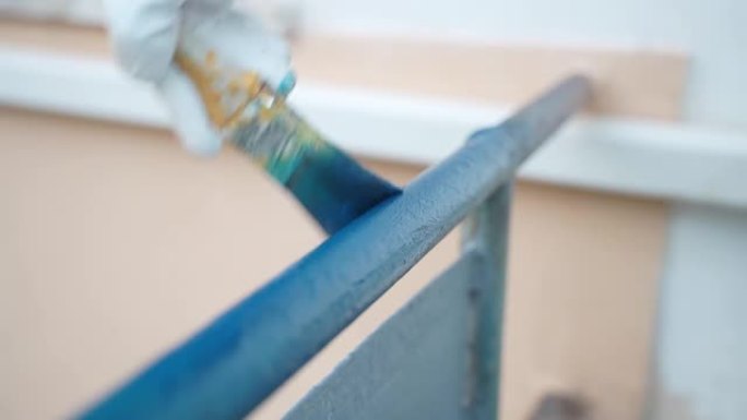 人手工作手套用画笔涂蓝色金属表面，修理工用保护性化学溶液更新侵蚀阳台框架，改善室外金属表面