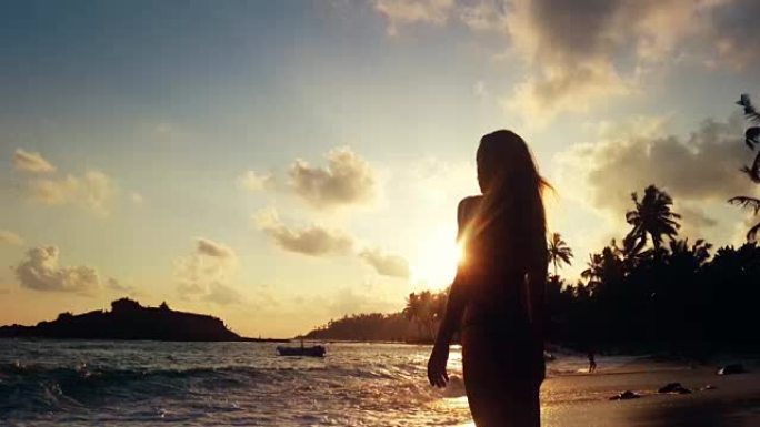 年轻女性在热带海滩观看日落，暴风雨的海浪洗沙