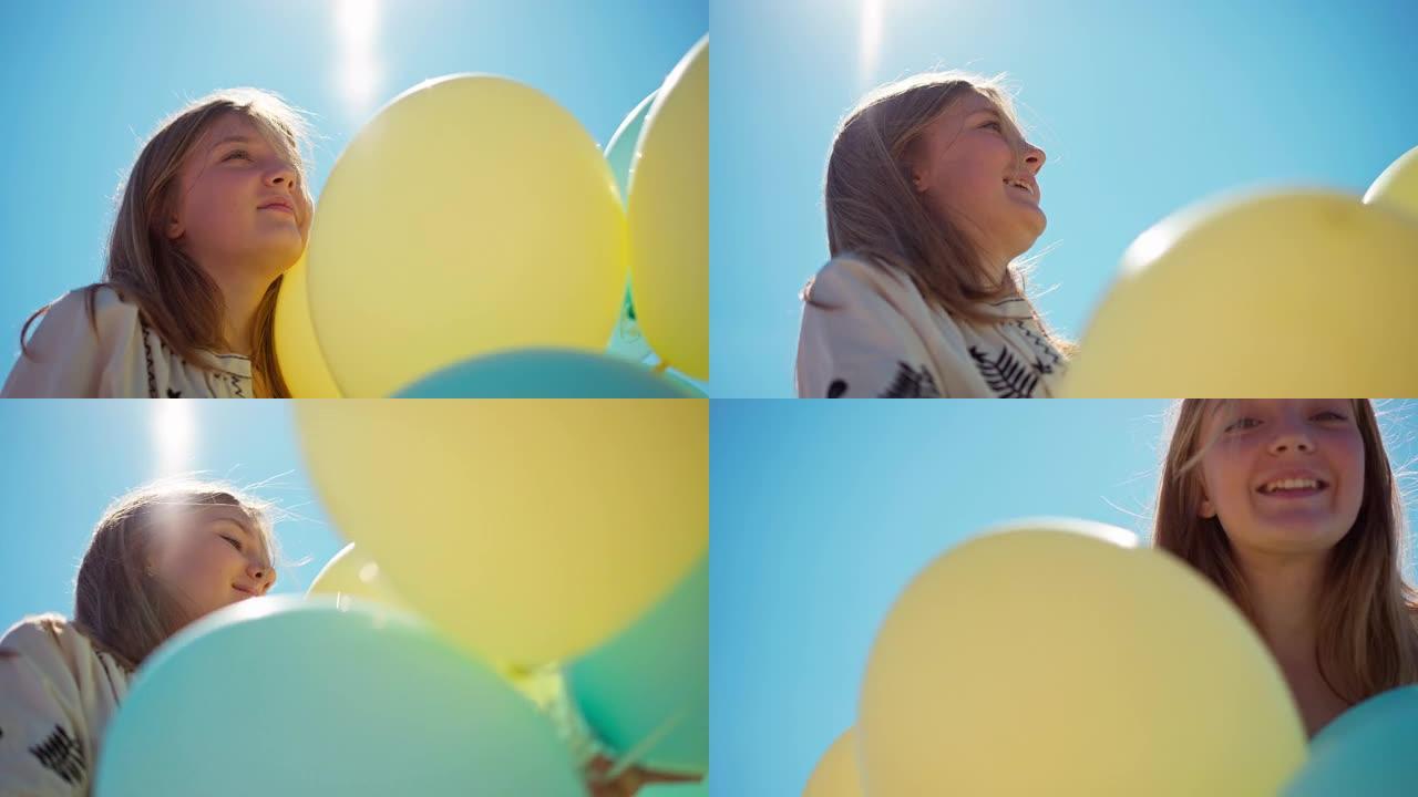底角视图开朗的少女与黄色和蓝色的气球在户外阳光。在无云的夏日春天天空笑的背景下，快乐微笑的少年肖像。
