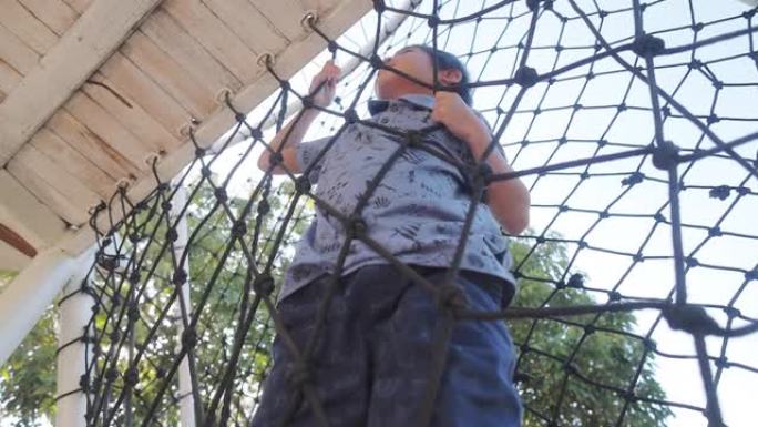 在儿童游乐场公园爬绳梯或网的男孩