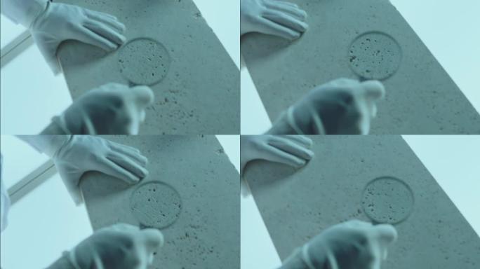 施工实验室检测天然钙华石的质量密度。实验室工作人员用放大镜探测石头。戴手套的手的特写视图。由ARRI