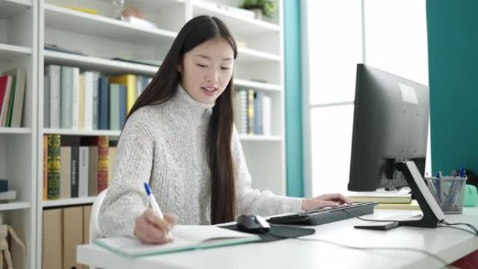 在图书馆大学使用笔记本电脑书写的年轻中国女学生