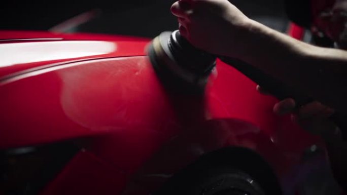 在清洗和细节车辆后，使用电动抛光机在美丽的红色跑车的挡泥板上工作的专业汽车美容师的特写镜头