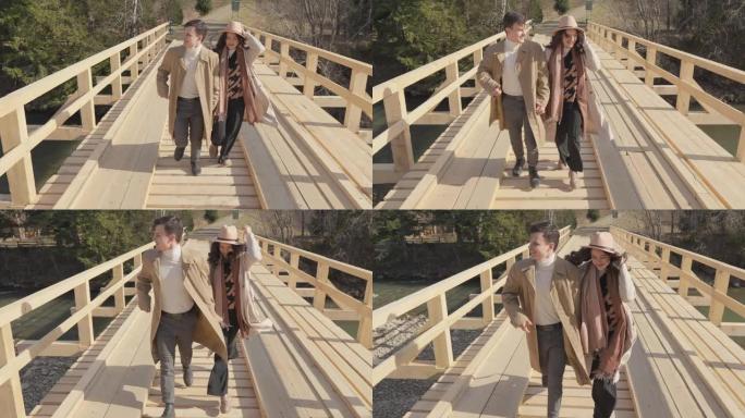 男孩和女孩在山上河上的木桥上奔跑。快乐无忧无虑的年轻夫妇，男人和女人玩得开心，浪漫而积极地休息，快乐