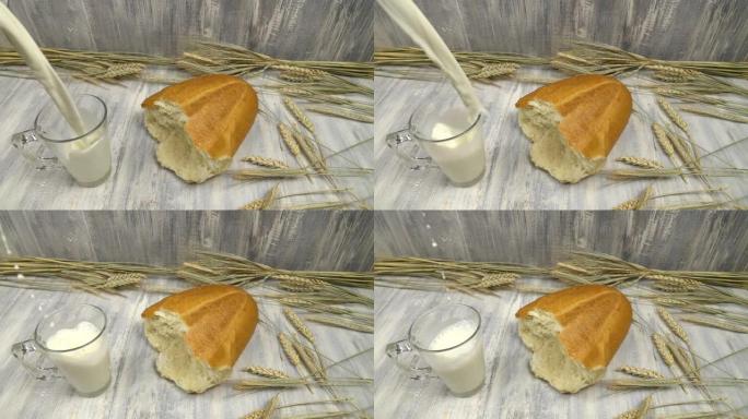 牛奶倒入玻璃杯中，玻璃杯放在麦穗和面包旁边的桌子上，慢动作