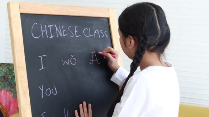 可爱的快乐亚洲女孩，长发编成辫子，在教室里学习汉语，学生孩子在黑板上练习写汉字，学习语言。