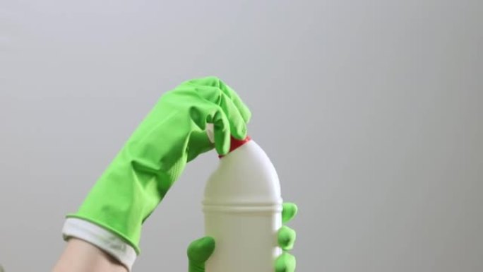 手持绿色橡胶手套，手持塑料洗涤剂瓶和开口盖