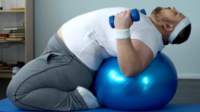 有动力的胖男举哑铃躺在健身球上，减肥计划