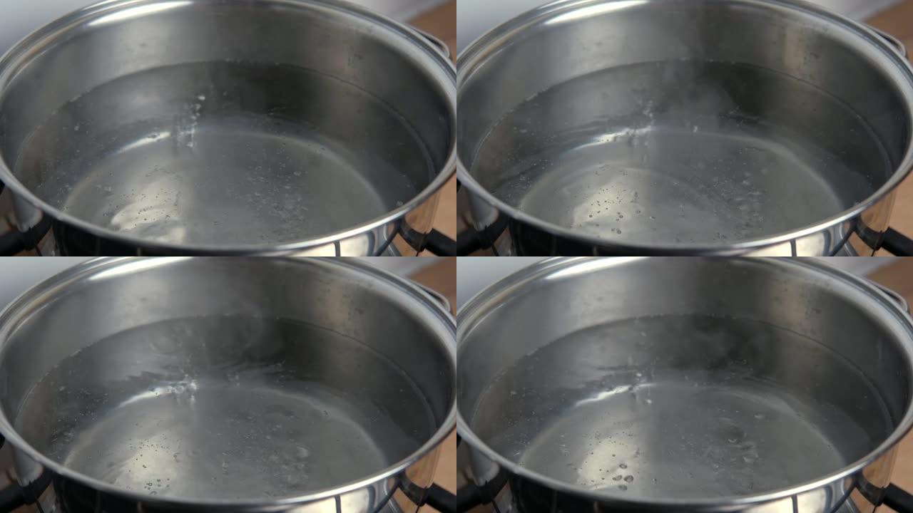 在热锅中清洗沸水。一锅开水，在现代厨房背景下有许多气泡。慢动作镜头。高角度特写。透明的水在燃烧的炉子