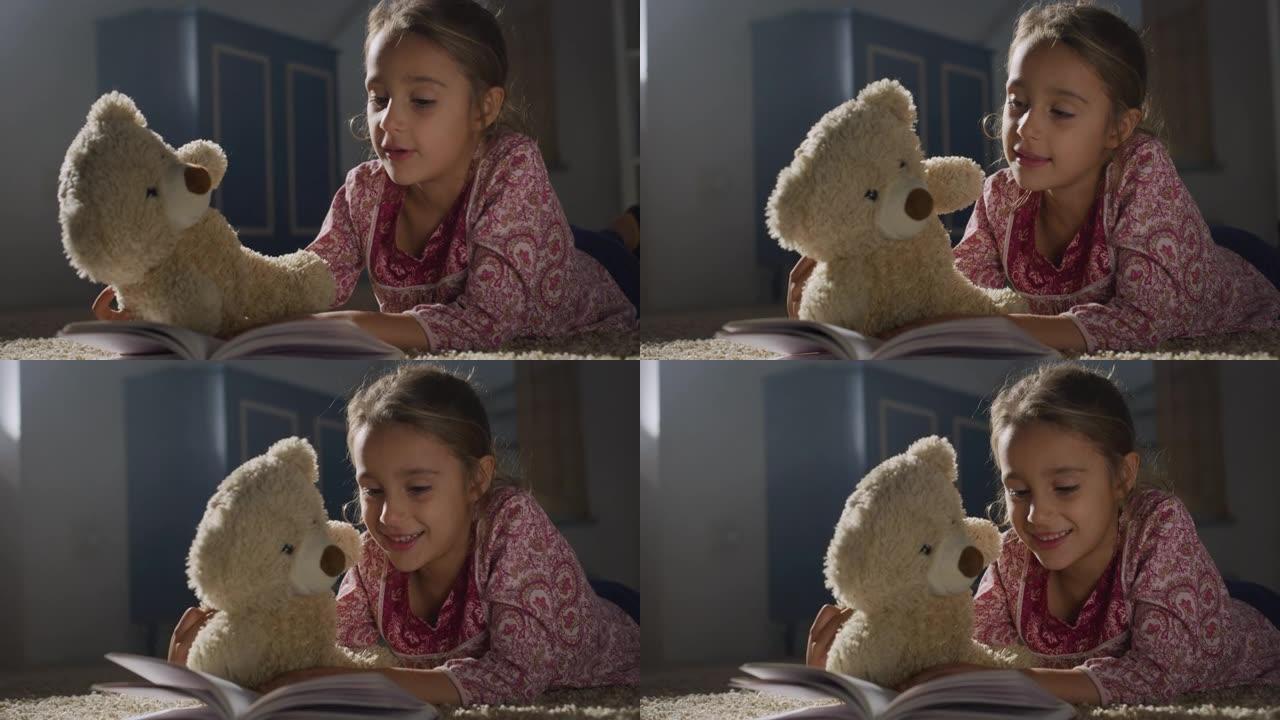 一个小女孩的肖像在晚上给她最喜欢的泰迪熊看书。快乐可爱的女孩玩她的玩具，讲故事。舒适氛围的童年概念