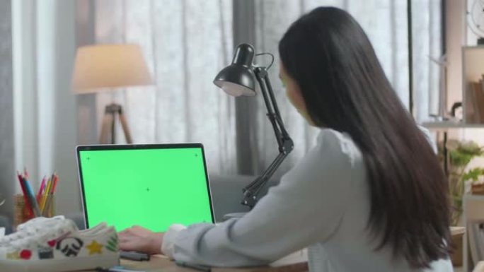 亚洲女鞋设计师在家中使用带有模拟绿屏的笔记本电脑