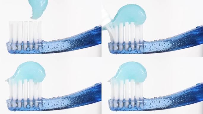牙刷和牙膏。蓝色牙刷的宏观视图，蓝色牙膏被挤压在白色背景上。慢动作