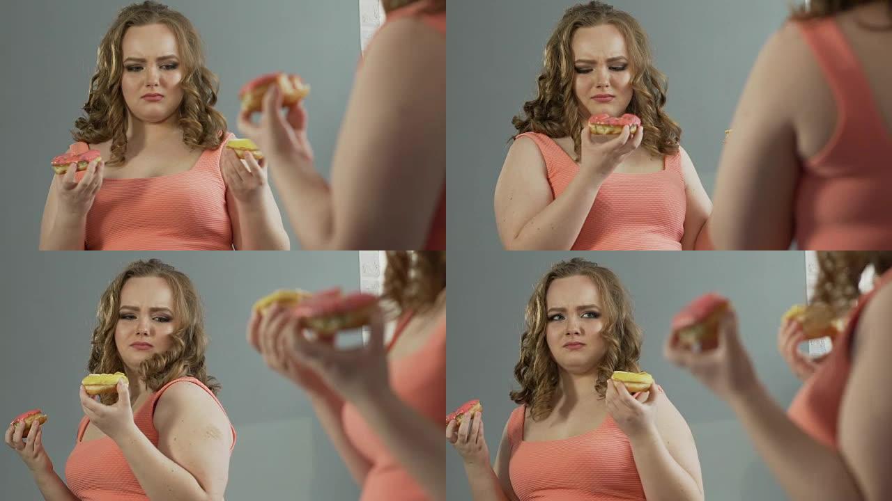 年轻的女士鄙视自己在镜子里超重的身体，同时吃甜甜圈