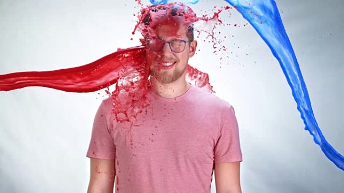 戴着眼镜的SLO MO LD年轻人在被蓝色和红色油漆击中时微笑