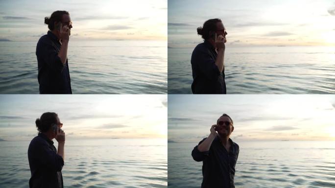 年轻人在日落时使用带有海水背景的电话
